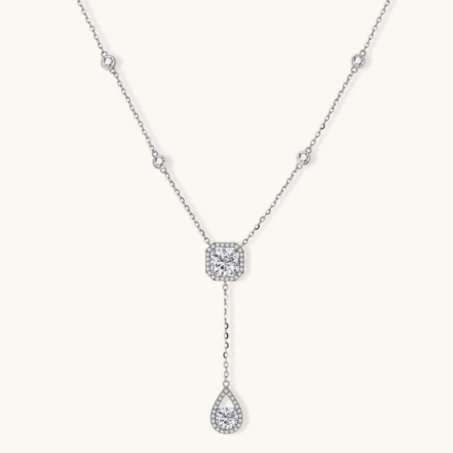 Sterling silver necklace with cushion-cut moissanite in halo setting and teardrop pendant, displayed on cream background.
