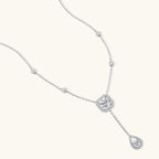 Sterling silver necklace with cushion-cut moissanite in halo setting and teardrop pendant, displayed on cream background.