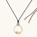 Geometric circle pendant necklace with crystal cluster on adjustable black cord, available in gold and silver finishes.