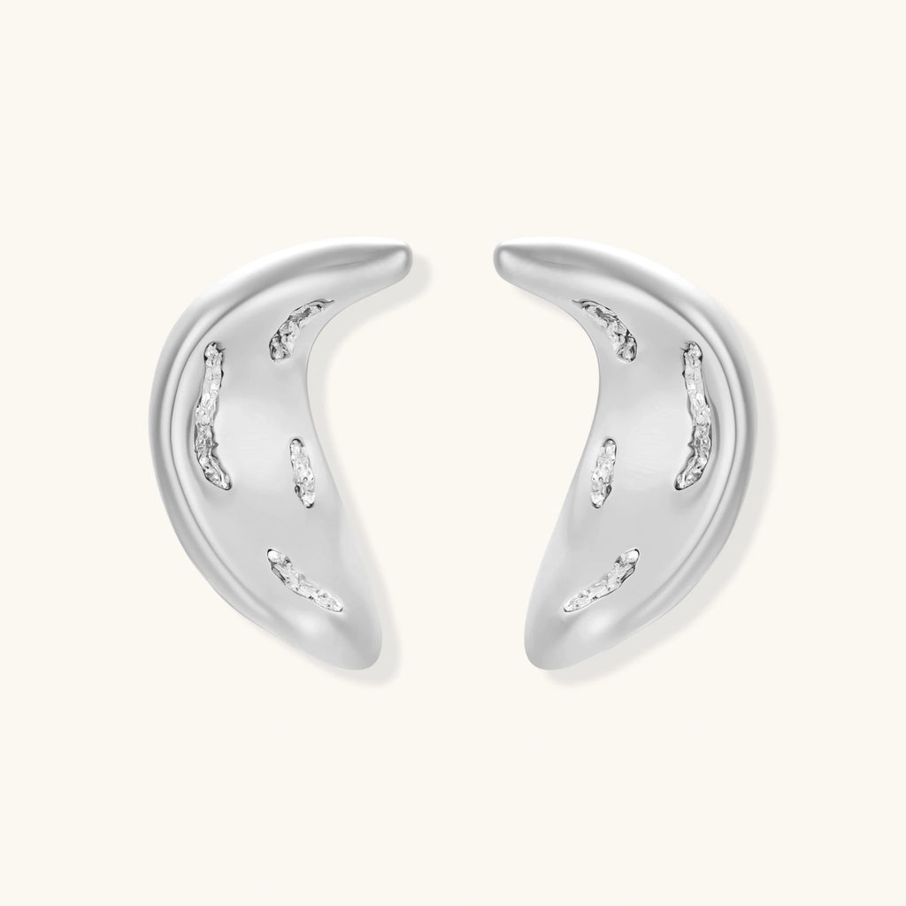 Curved crescent-shaped earrings in gold and silver with scattered perforated details on neutral background.