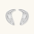Curved crescent-shaped earrings in gold and silver with scattered perforated details on neutral background.