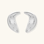 Curved crescent-shaped earrings in gold and silver with scattered perforated details on neutral background.