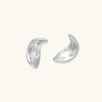 Curved crescent-shaped earrings in gold and silver with scattered perforated details on neutral background.