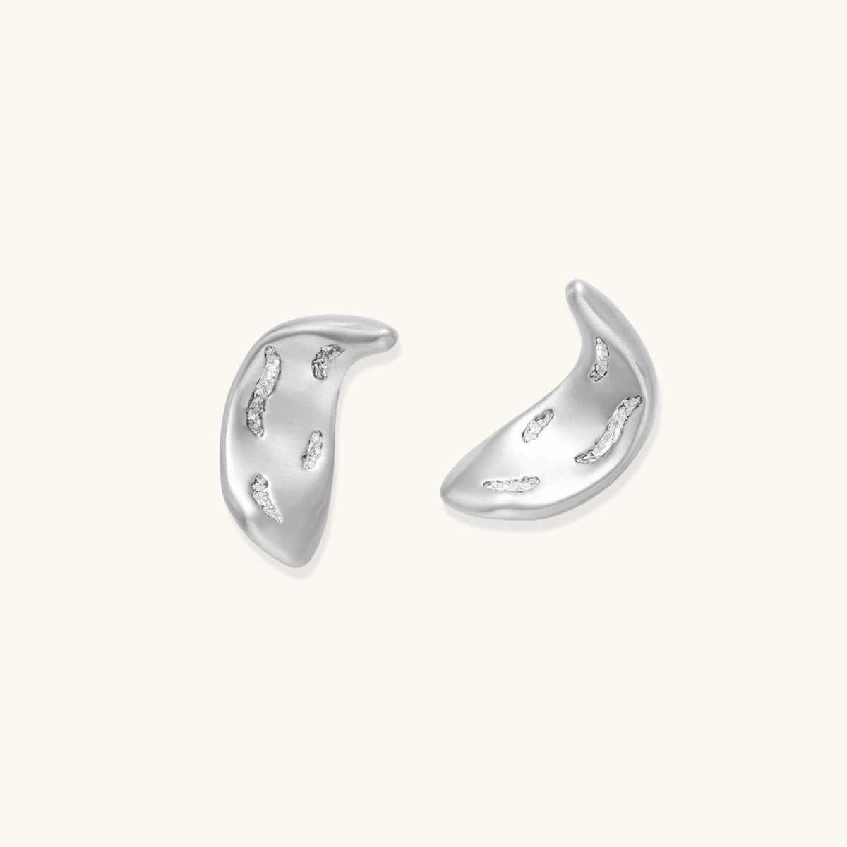 Curved crescent-shaped earrings in gold and silver with scattered perforated details on neutral background.