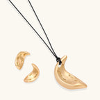 Gold-toned crescent moon pendant with textured surface on black adjustable cord, displayed with matching crescent earrings