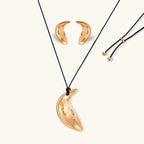 Gold-toned crescent moon pendant with textured surface on black adjustable cord, displayed with matching crescent earrings