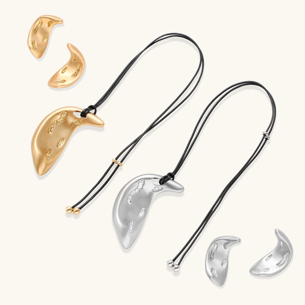 Gold-toned crescent moon pendant with textured surface on black adjustable cord, displayed with matching crescent earrings