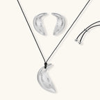 Crescent moon shaped pendant and earrings in eco-zinc alloy with curved crystal inlay patterns on light background.