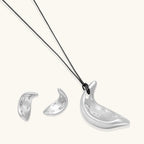 Crescent moon shaped pendant and earrings in eco-zinc alloy with curved crystal inlay patterns on light background.