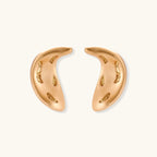 Pair of gold crescent moon-shaped stud earrings with textured surface details on cream background.