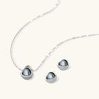 Silver gray Tahitian-style pearl pendant necklace and matching pave zirconia stud earrings set on cream background.