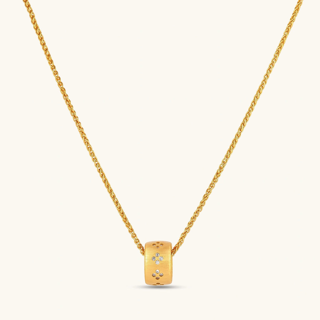Gold-plated cylindrical ring pendant with brushed finish and scattered crystal accents on a wheat-link chain, cream background.