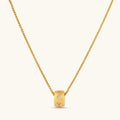 Gold-plated cylindrical ring pendant with brushed finish and scattered crystal accents on a wheat-link chain, cream background.