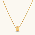 Gold-plated cylindrical ring pendant with brushed finish and scattered crystal accents on a wheat-link chain, cream background.
