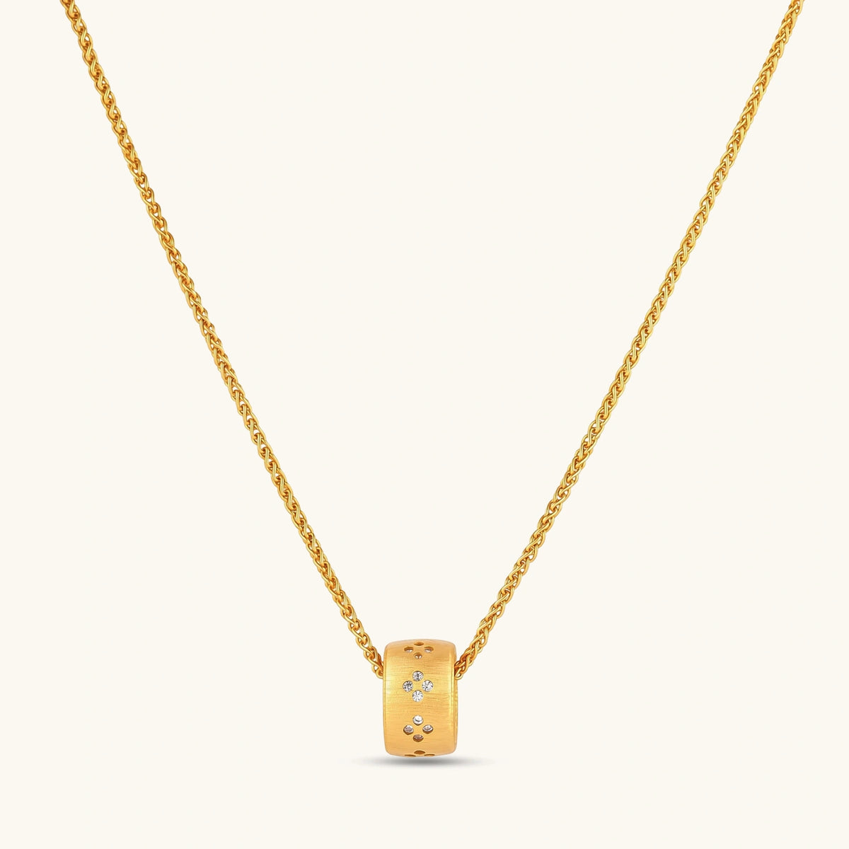 Gold-plated cylindrical ring pendant with brushed finish and scattered crystal accents on a wheat-link chain, cream background.