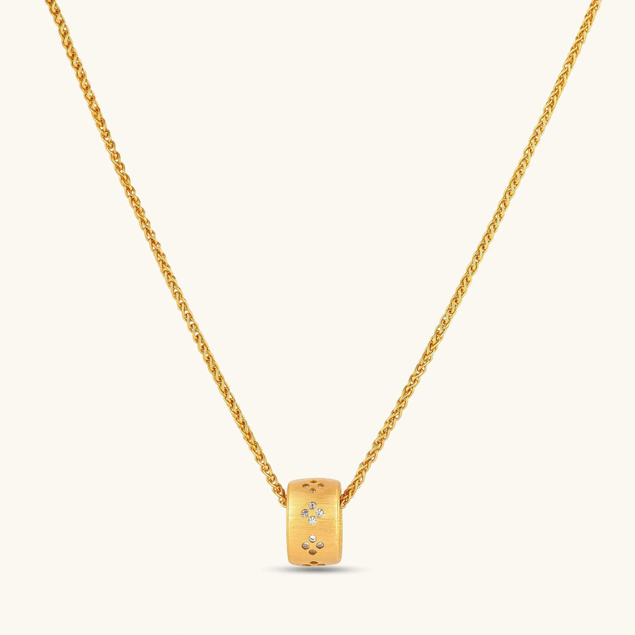 Gold-plated cylindrical ring pendant with brushed finish and scattered crystal accents on a wheat-link chain, cream background.
